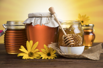 Honey dripping from a wooden honey dipper in a jar on wooden background