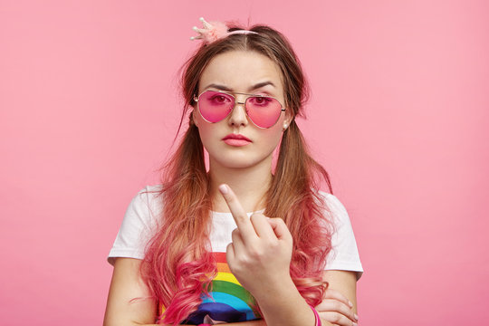 Naughty impudent female look stylish, flipps off or shows middle finger, has indifferent attitude what people think about her, has dispute with someone. Rude ignorant ill mannered girl in pink glasses