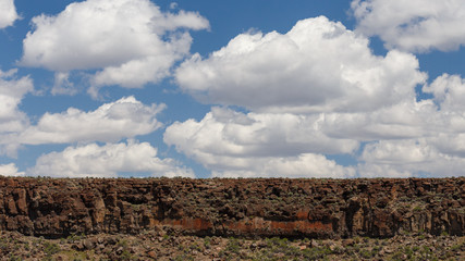 Desert rock cliff landscape with varied cracked rock patterns and puffy cloud background mixed with blue sky.