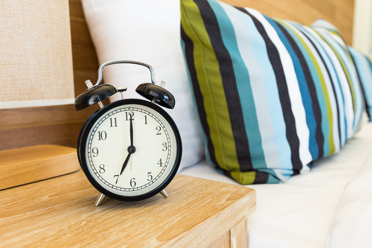 Vintage retro alarm clock on bed side table at 7 o'clock