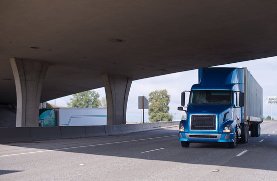 Big rig blue semi truck going under bridge