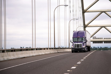 Lilac modern big rig semi truck with trailer moves along the arch bridge to deliver commercial cargo