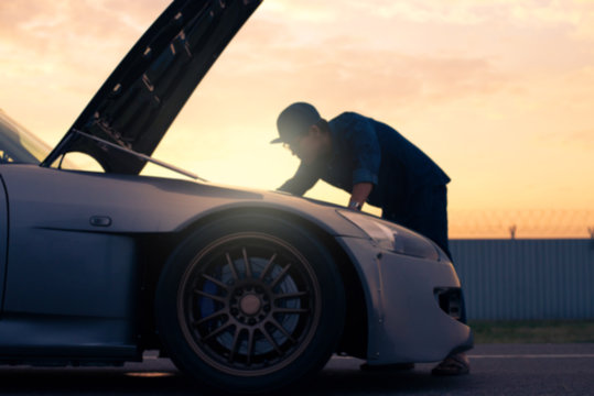 Abstract blurred background of man is checking engine bay of sport car while sunset.
