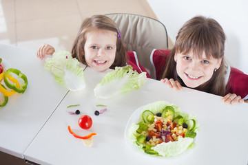 Happy girls making funny salad faces. Cooking vegetarian meal