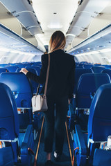 Back view of young woman wearing formal suit walking the aisle on plane