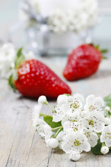 Strawberries and blooming hawthorn flowers on rustic wooden table.