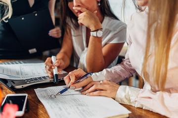 Close-up view of young women working on accounting paperwork checking and pointing at documents sitting at desk in office