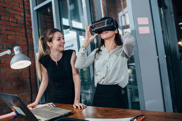 Two female application developers testing a new app designed for VR headset standing in modern...