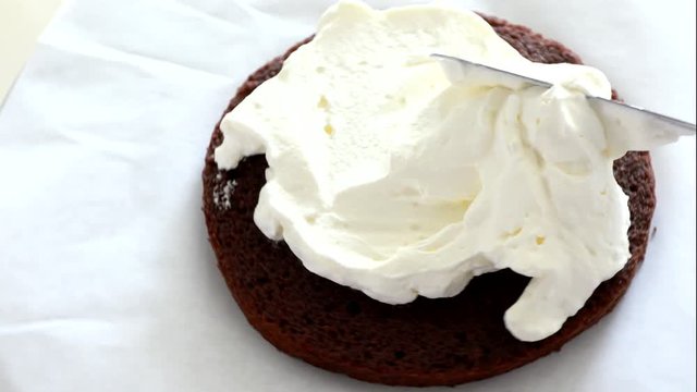Woman's hand spreading whipped white cream on chocolate sponge cake