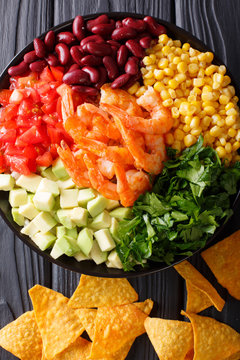 Mexican salad with shrimps, beans, corn, avocado and greens close-up. Vertical top view