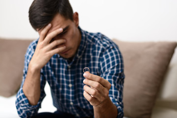 Divorce concept. Sad lonely man holding engagement ring sitting at home. Depression after a divorce. Selective focus.