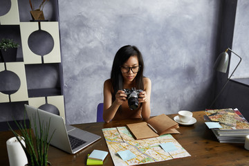 Beautiful young Korean female travel blogger sitting at home office with map, portable computer and...