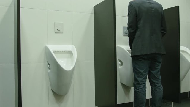 Man peeing to toilet bowl in restroom. Long shot