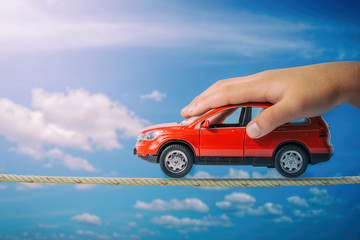 Red car in hand child on rope with blue sky background. Driving safety concept