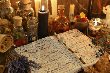 Magic book with spells, lavender bunch and black candle on witch table.