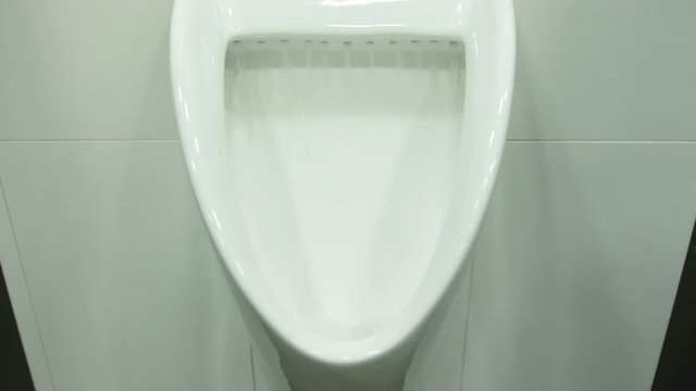 A white urinal in men's public toilet. Flushing down. Close-up shot