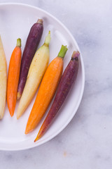 Heirloom rainbow carrots in a white dish. Marble tabletop/background