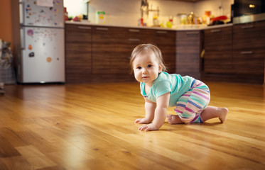 Cute smiling little baby girl crawling on the floor at kitchen. Seven month old infant child at home