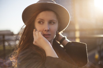 Outdoor portrait. Young stylish beautiful woman in hat speaking on phone while walking in the big city streets. 