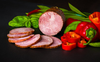 Smoked sausage, ham with red and green peppers and herbs on a dark background