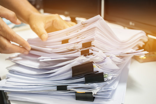 Businessman hands working in Stacks of paper files for searching information on work desk office, business report papers,piles of unfinished documents achieves with clips indoor,Business concept