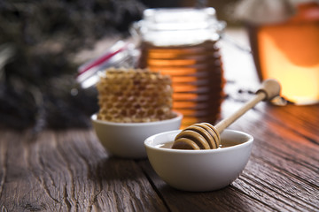 Honey dripping from a wooden honey dipper in a jar on wooden background