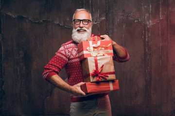 Handsome senior bearded man holding gift box over dark background and looking at camera. Santa Claus wishes Merry Christmas and a happy new year.