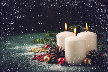 Three Christmas burning candles and decorations on dark turquoise background