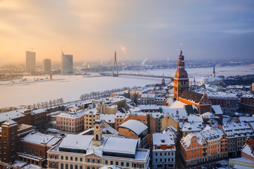 Fototapeta premium View of the roofs of the old city and the tower of the Dome Cathedral against background of an ice-covered river. Winter evening in Riga. Latvia.