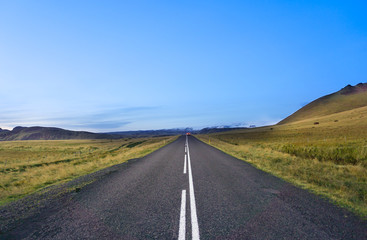 middle of th road with green field and blue sky in Iceland without car