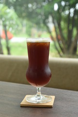 Glass of ice black tea on the desk front window   
