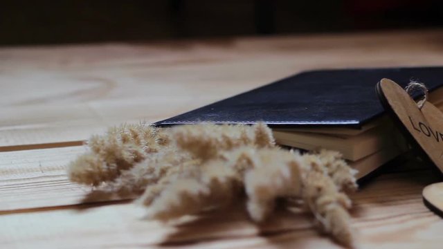 Love composition on a wooden table. The book, spikelets of a golden plant, a cup of tea, hearts on a wooden table