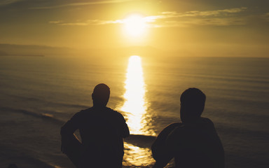 Naklejka premium Para facet na tle plaża ocean wschód słońca, sylwetka dwie osoby przytulające się i patrząc widok wieczorny krajobraz morski, romantyczni przyjaciele hipster razem cieszyć się zachodem słońca, podróże wakacje wakacje, koncepcja relaksu