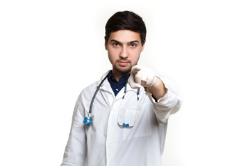 Fototapeta premium beautiful young doctor in a dressing gown with a stethoscope on a white background in the studio, points at you, sign