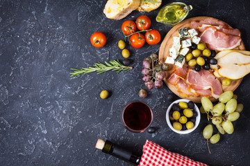 Fototapeta na wymiar Appetizer, italian antipasto, ham, olives, cheese, bread, grapes, pear and wine on dark stone background. Top view