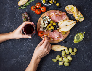 Woman hands hold a glass of wine. Appetizer, italian antipasto, ham, olives, cheese, bread, grapes,...
