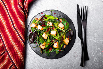 Warm pumpkin salad with mixed leaf of arugula, chard, in on black slate plate on grey background. Grilled pumpkin. Top view