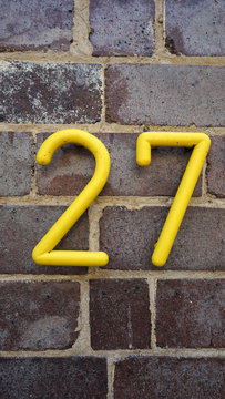 House number on the brick wall - twenty seven (27) in yellow numerals