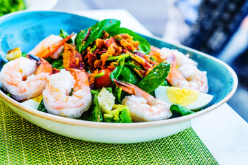 Fresh salad with prawns, avocado and mixed greens on the plate and green napkin close up. Healthy food.