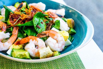 Fresh salad with prawns, avocado and mixed greens on the plate and green nupkin close up. Healthy food.
