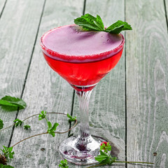 Classic frozen alcoholic cold drink with ice, raspberry, mint, martini and vodka in a glass. Cocktail with alcohol and fruit juice on a wooden table.