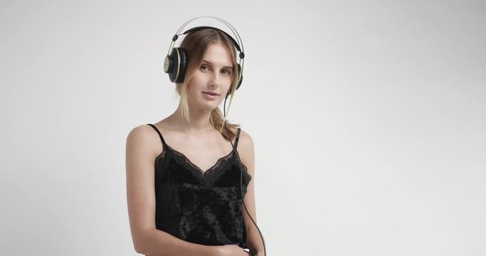 Blond young woman in headphones and black lacy camisole listening to music in headphones and dancing
