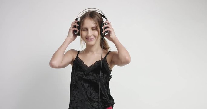 Sexy young girl in black cami and red boxers putting on headphones and starting to dance isolated on white