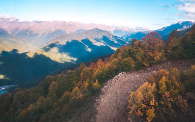 Ski tracks and colorful autumn forests covering slopes of Caucasus mountains on bright sunny day. Krasnaya Polyana, Russia