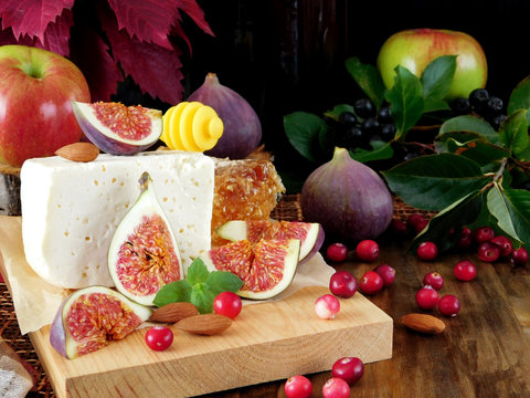 Cheese made of sheep milk and slices of figs on a wooden board surrounded by cranberries, honey and almond. Ingredients for a cheese plate