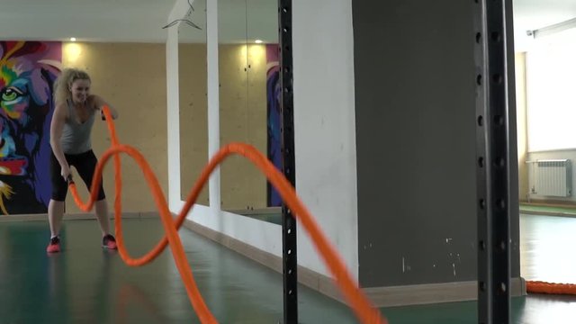 A young athletic woman in tonus works with combat ropes in the gym. Slow motion