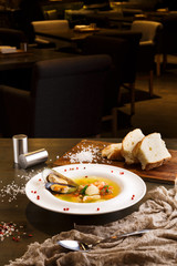 French seafood soup with white fish, shrimps and mussels in plate at wooden background