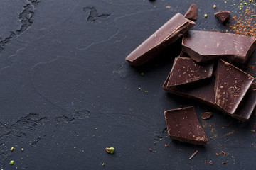 Broken chocolate pieces and cocoa powder on black background