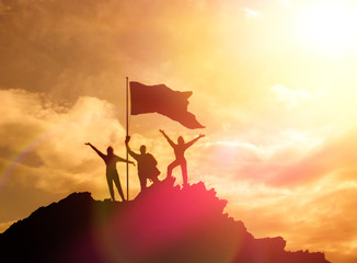 High achiever, silhouettes of three people holding on top of a mountain to raise their hands up. A...