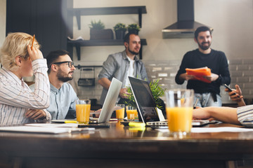 Group of creative coworkers brainstorming at kitchen. Business people working together and using laptops. Young team of managers making great business discussion in modern loft. Teamwork concept
